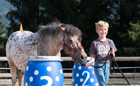 Junge führt geflecktes Pony an blauen Fässern mit Zahlen 2 und 3 im Freien
